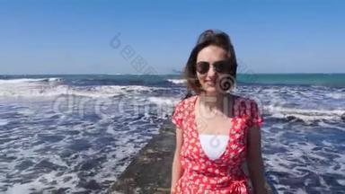 年轻可爱的女人微笑着走在海上<strong>码头</strong>上。 强烈的波浪在背景上撞击和<strong>飞溅</strong>。